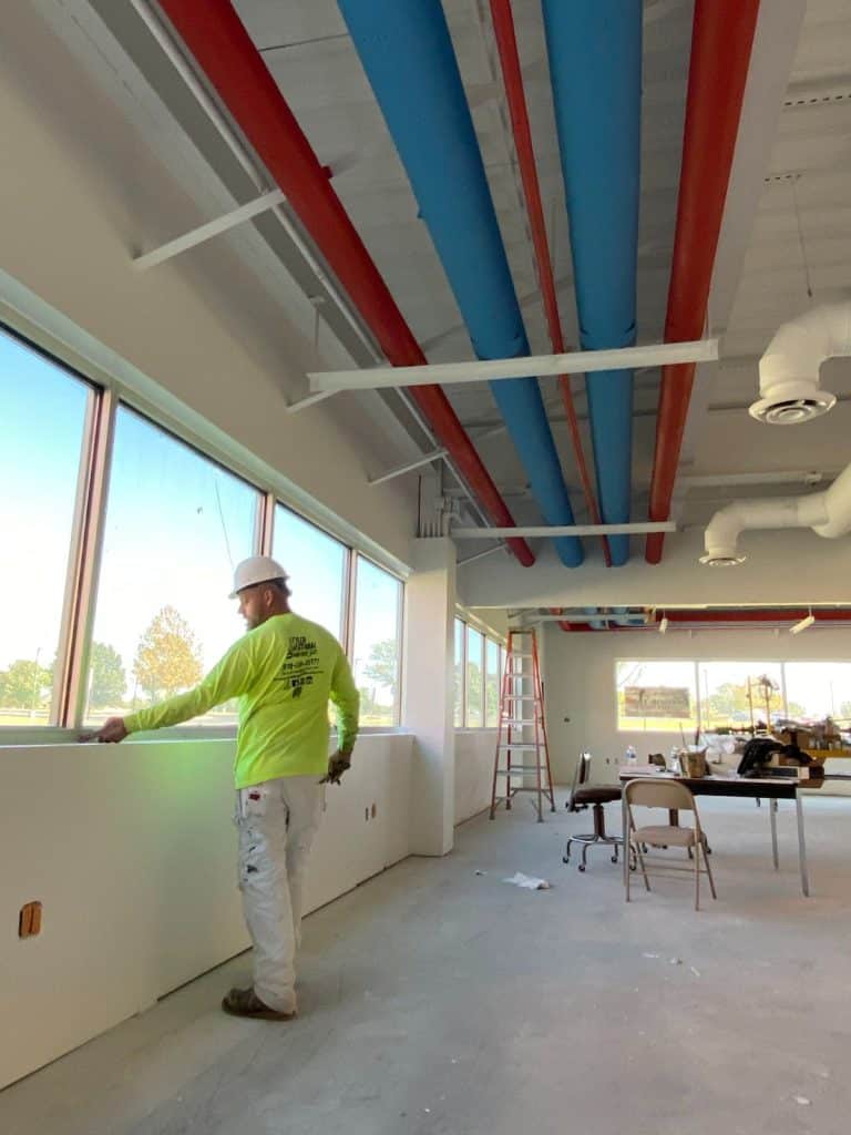 TCCCyberSecurityLab3 Painter inspecting interior wall with exposed red and blue ceiling pipes.