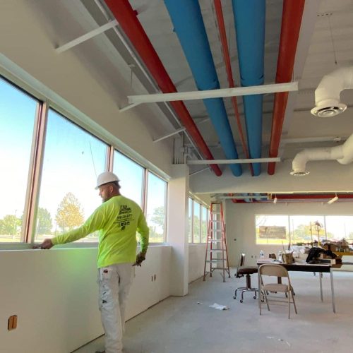Worker painting interior walls with exposed ceiling pipes